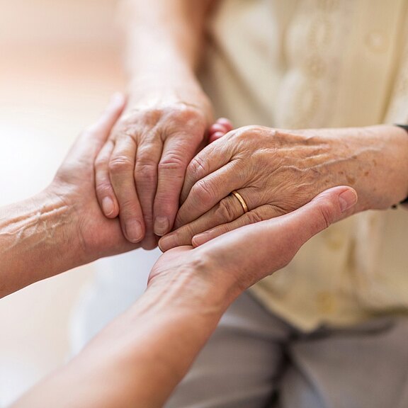 Nahaufnahme: Eine Person hält sanft die Hände einer älteren Person – Ausdruck von Fürsorge, Trost und Unterstützung.