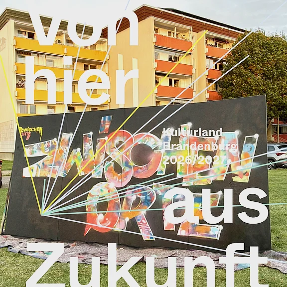 Foto einer Außentafel. Großtypografie mit dem Slogan Von hier aus Zukunft. Auf der Tafel steht bunt ZWISCHENRÄUME. Rechts kleiner Kulturland Brandenburg 2026/2027. Das Bild wirbt für ein Kulturprojekt und betont Zukunftsperspektiven und Zwischenraumthemen.