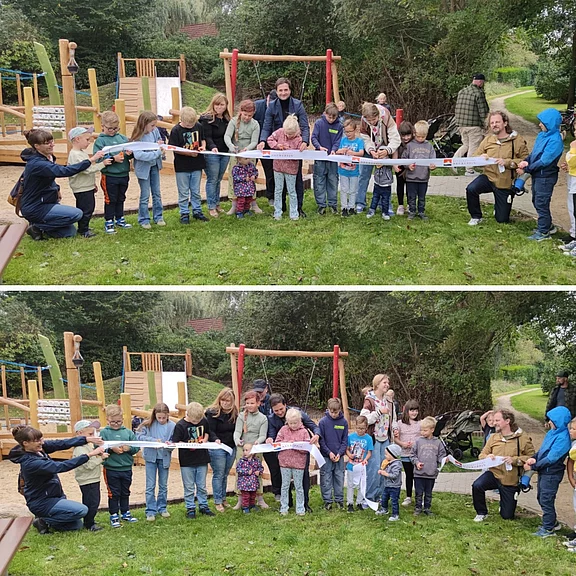 Eine Gruppe von Kindern und Erwachsenen steht im Freien vor einem neuen Spielplatz. Sie halten ein großes Band, das durch geschnitten werden soll, um den Spielplatz einzuweihen. Die Beteiligten wirken freundlich und feiern diesen besonderen Moment.