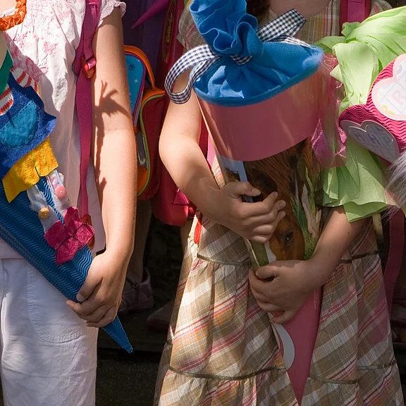 Nahaufnahme von Kindern am ersten Schultag: Sie halten bunte, große Schultüten und tragen Rucksäcke. Die Bildausschnitte zeigen nur ihre Oberkörper und Arme. Stimmung festlich, Fokus auf den farbenfrohen Zuckertüten als Symbol für den Schulstart.